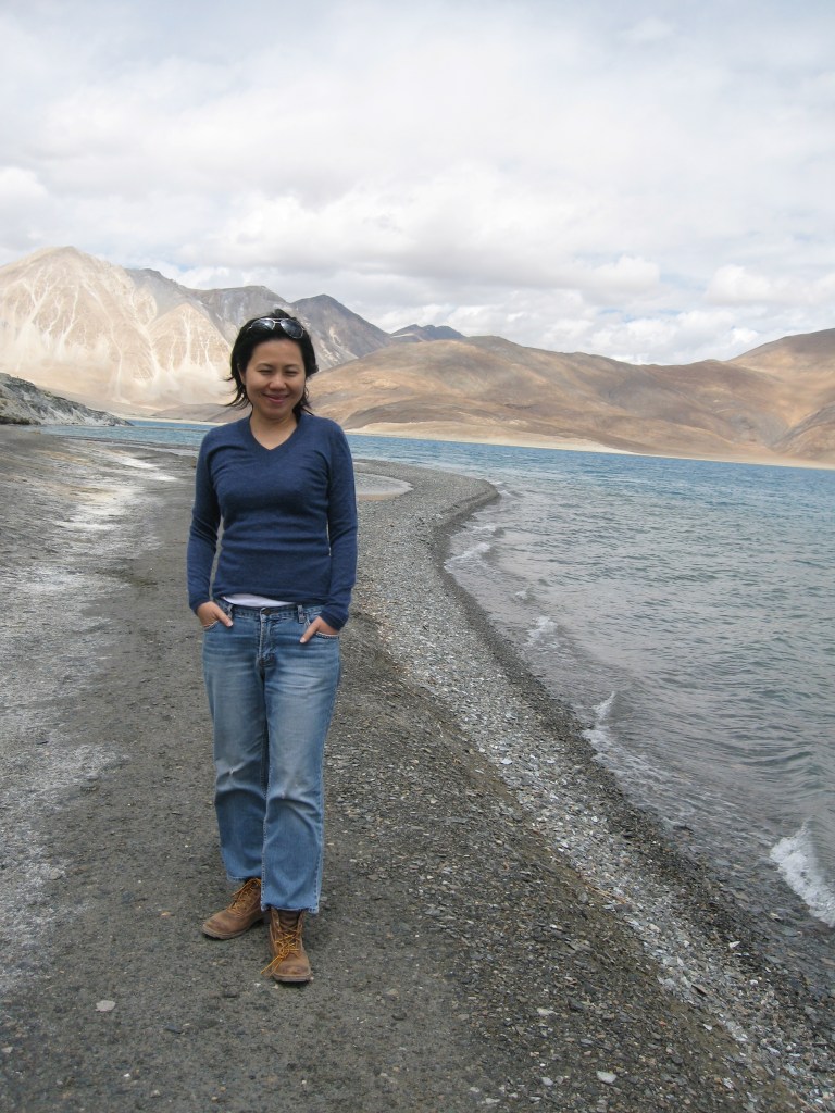 A person standing by the shore of a crystal-clear lake, surrounded by majestic mountains in a serene landscape.
