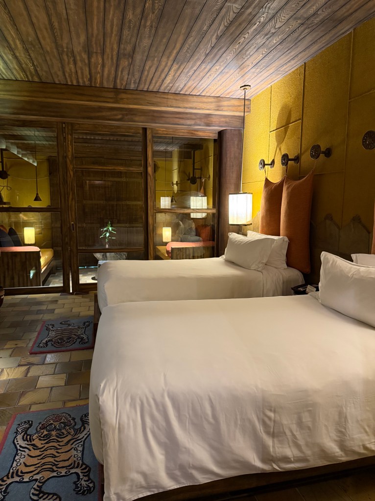 Interior view of a hotel room featuring two beds, wooden ceiling, and softly lit ambiance.