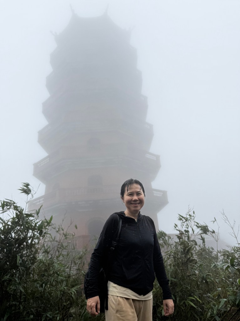 A person standing in front of a pagoda on a misty day at Yen Tu Mountain, surrounded by greenery.