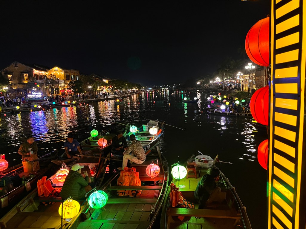 A view of boats on a river at night in Hoi An, Vietnam, decorated with vibrant lanterns reflecting in the water.