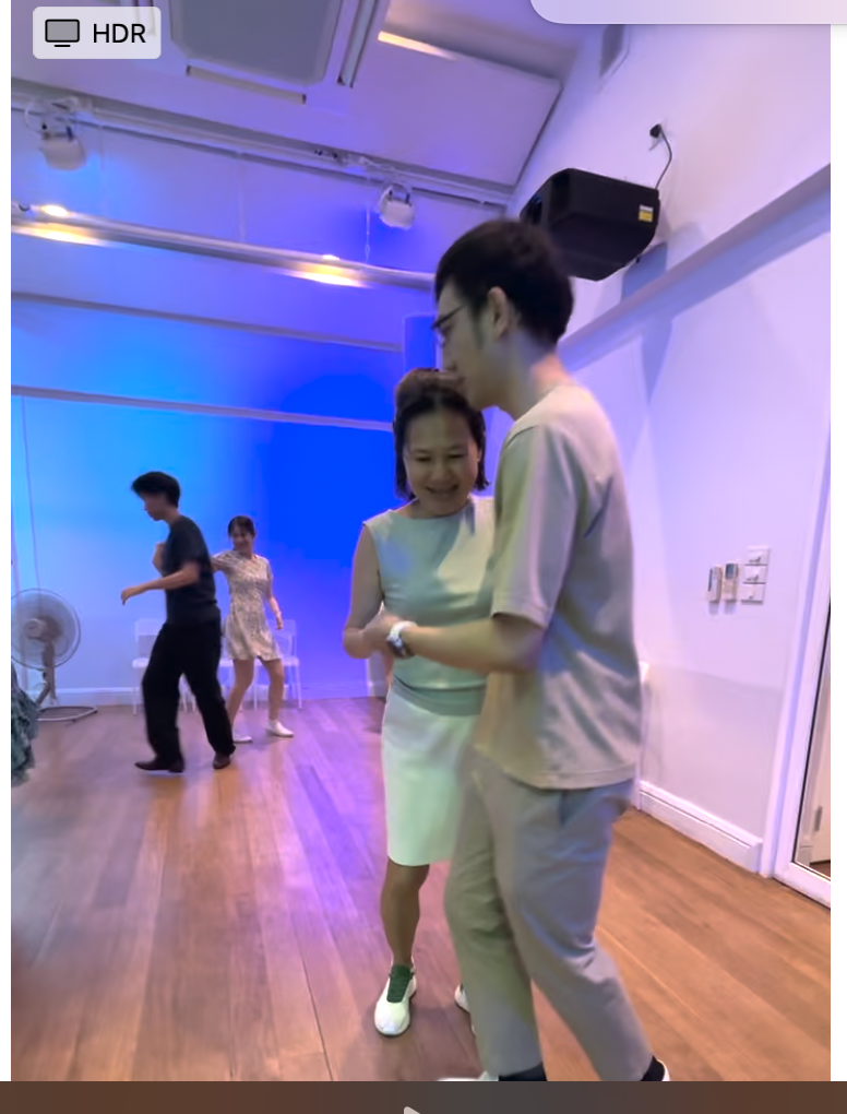 A couple is dancing closely in a well-lit venue with blue ambient lighting, surrounded by other people on the dance floor.