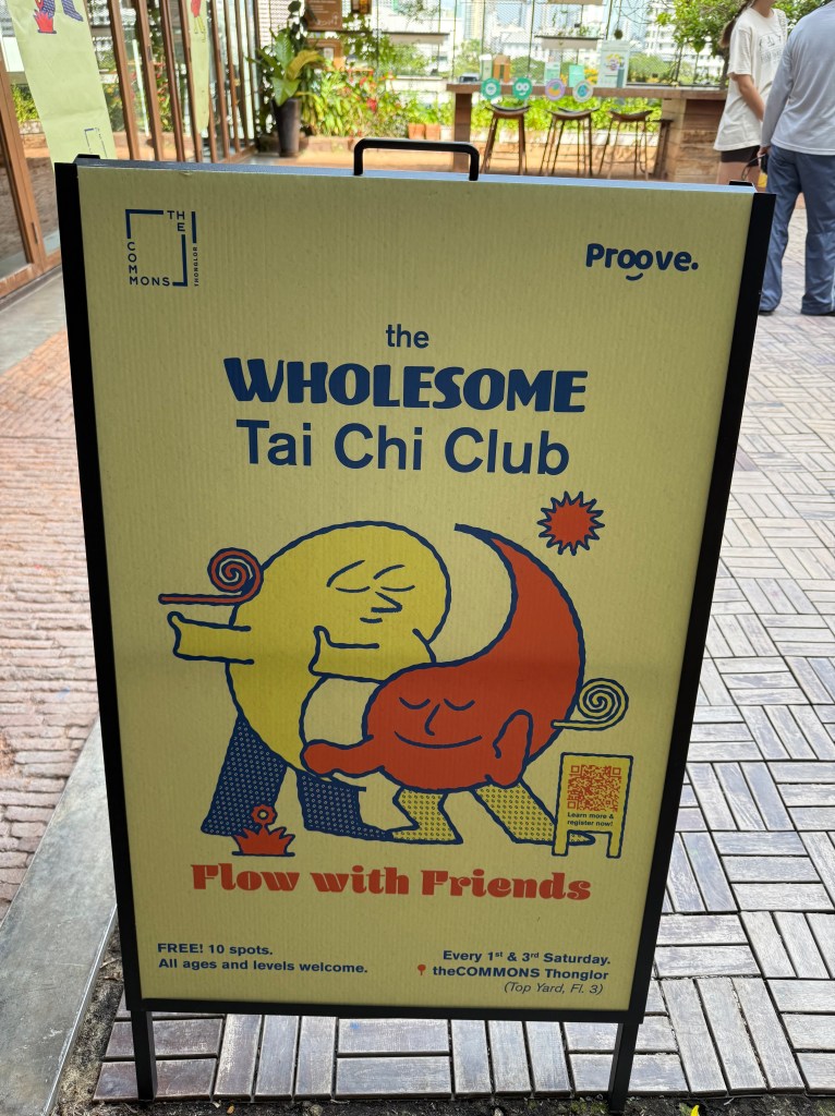 A colorful sign for the WHolesome Tai Chi Club at The Commons Thonglor, featuring playful illustrations and details about free Tai Chi sessions.