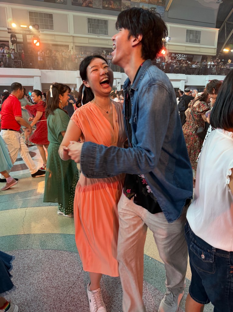 Two people joyfully dancing together in a lively event, surrounded by a crowd, conveying a sense of connection and happiness.