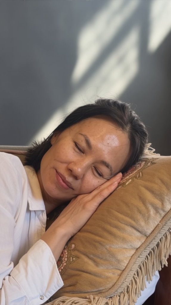 A woman resting peacefully on a decorative pillow, her eyes closed, showcasing a serene and relaxed expression.