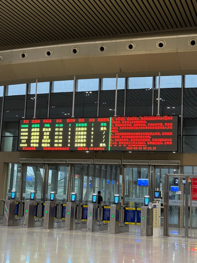 Interior of a modern train station in China, featuring a digital departure board with train information and several ticket gates.
