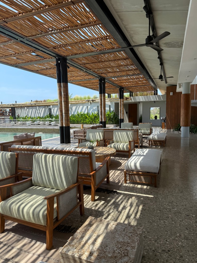 An elegantly designed lounge area at Cap Karoso resort in Sumba, featuring wooden furniture, plush seating, and a tranquil atmosphere illuminated by natural light filtering through a bamboo canopy.