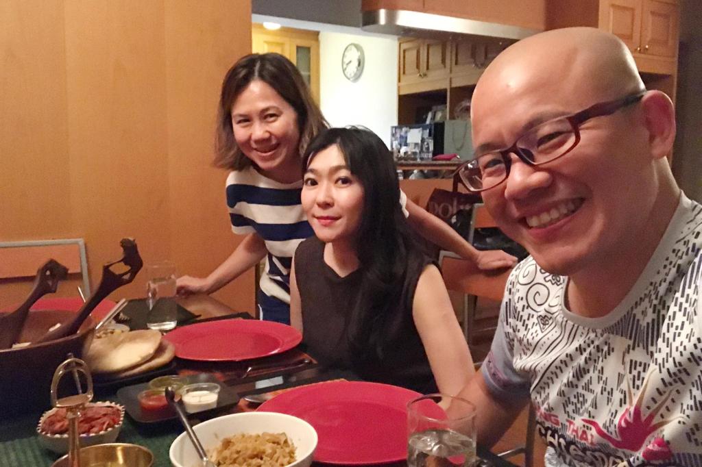 Three friends gathered around a dining table with plates of food, smiling and enjoying each other's company.