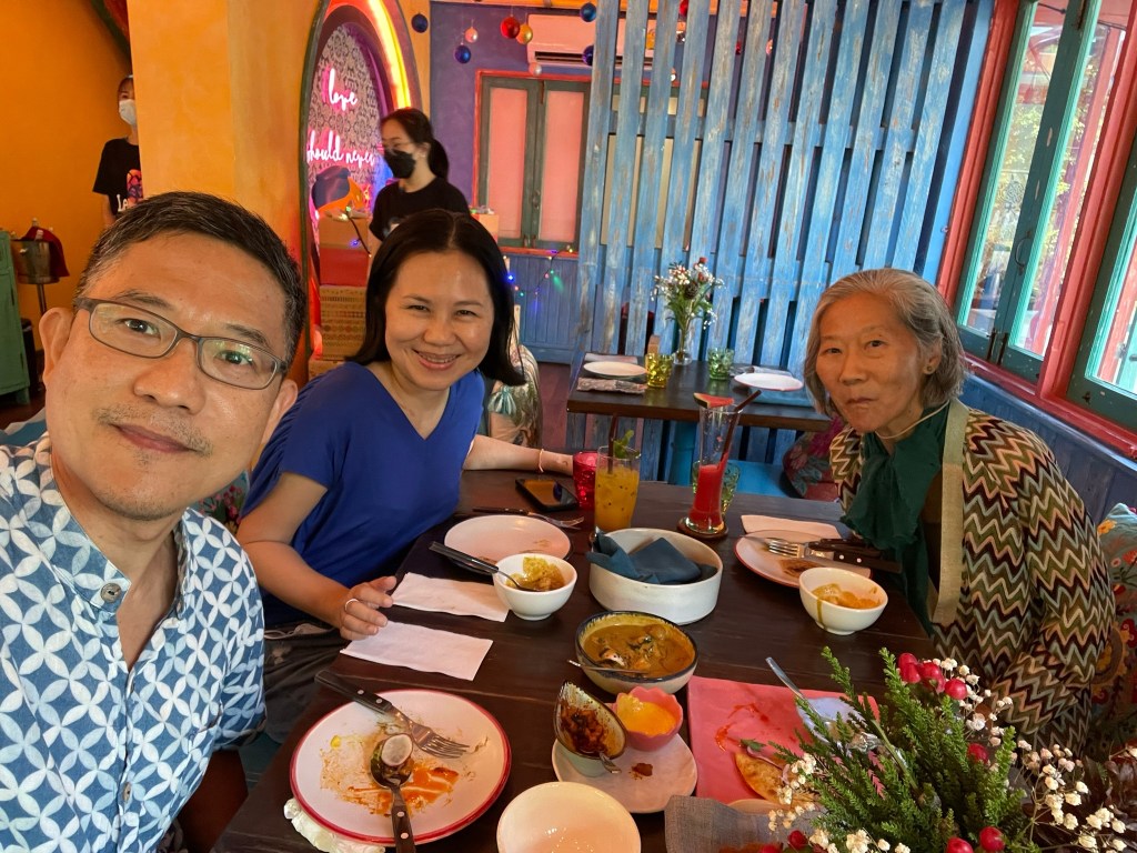 Three people smiling together at a colorful restaurant table with food and drinks, capturing a moment of friendship and connection.