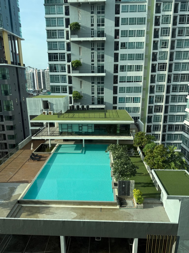 Aerial view of a residential condominium featuring a large swimming pool surrounded by greenery and modern architecture.
