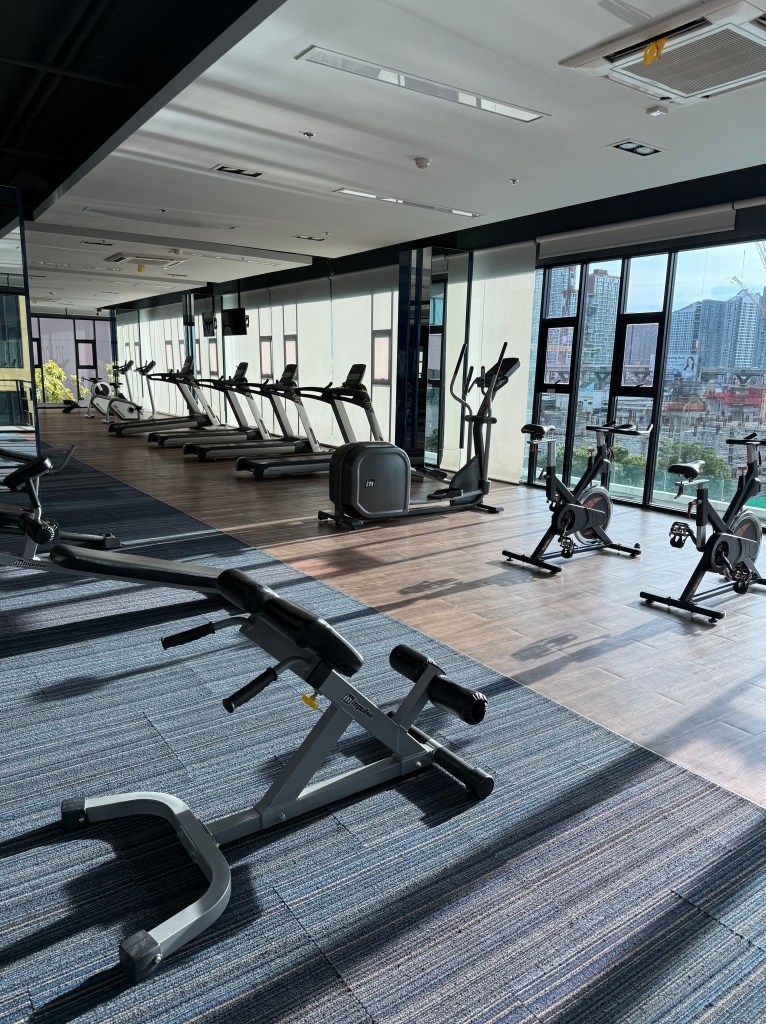 Interior view of a modern gym featuring various exercise equipment, including treadmills and stationary bikes, with large windows allowing natural light to illuminate the space.
