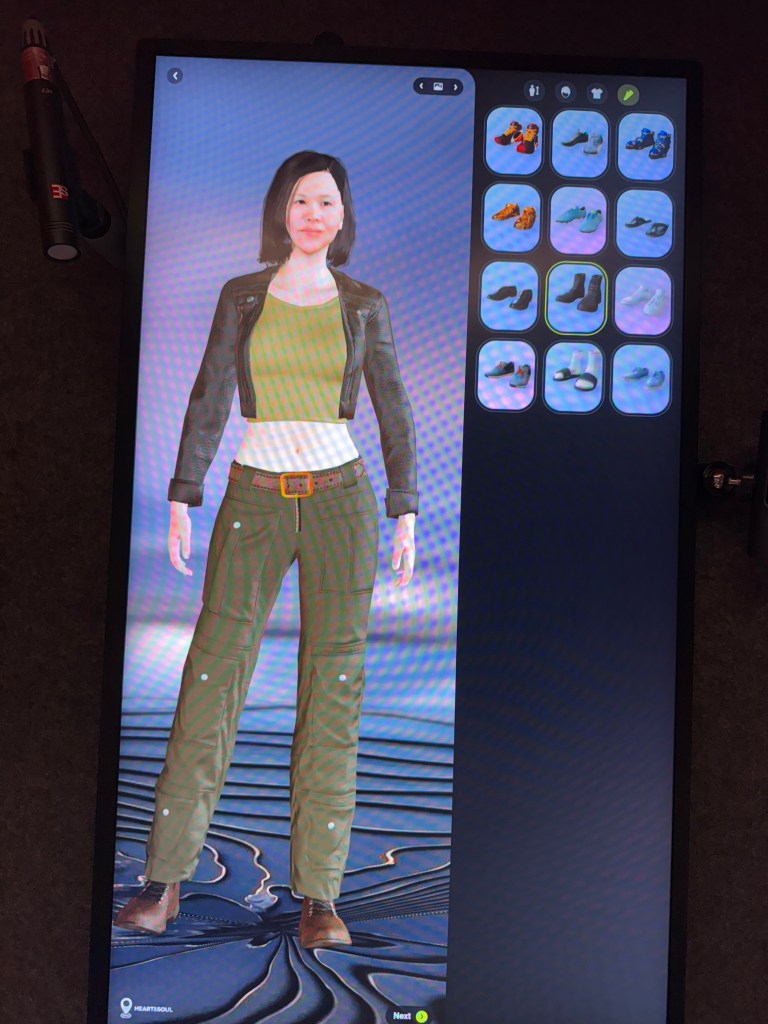 A digital avatar displaying a woman with short hair wearing a green top, black jacket, and green pants, alongside a selection of shoes on a touchscreen interface.