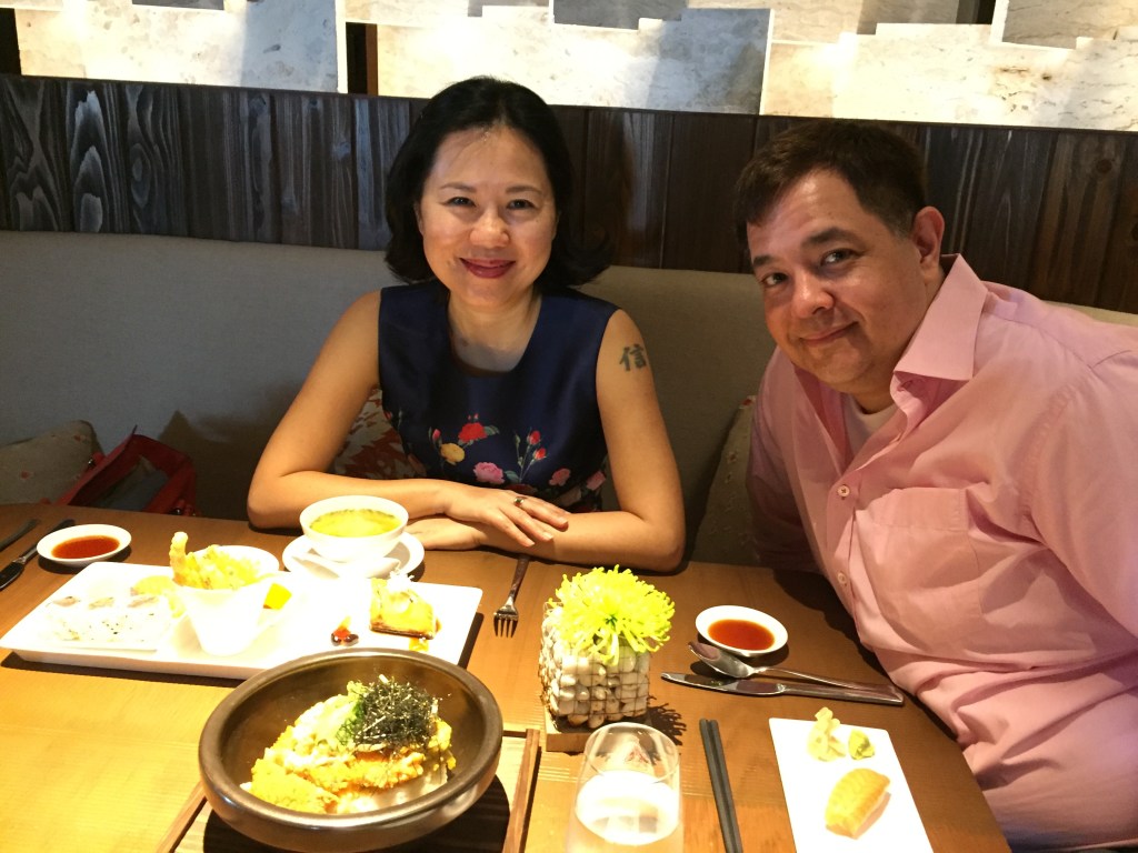 A smiling woman and man sitting at a table with various dishes of food, enjoying a meal together in a cozy restaurant setting.