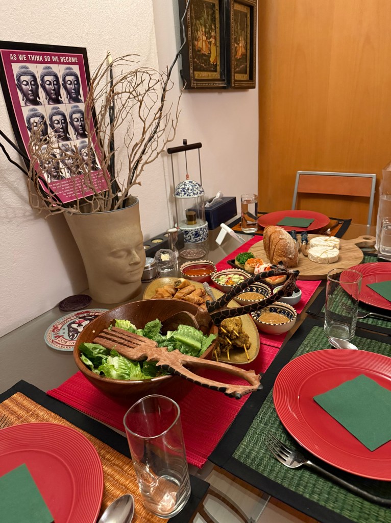 A beautifully set dining table featuring colorful plates, glasses, and a variety of dishes, including salad and traditional recipes, surrounded by decorative elements such as artwork and a vase.