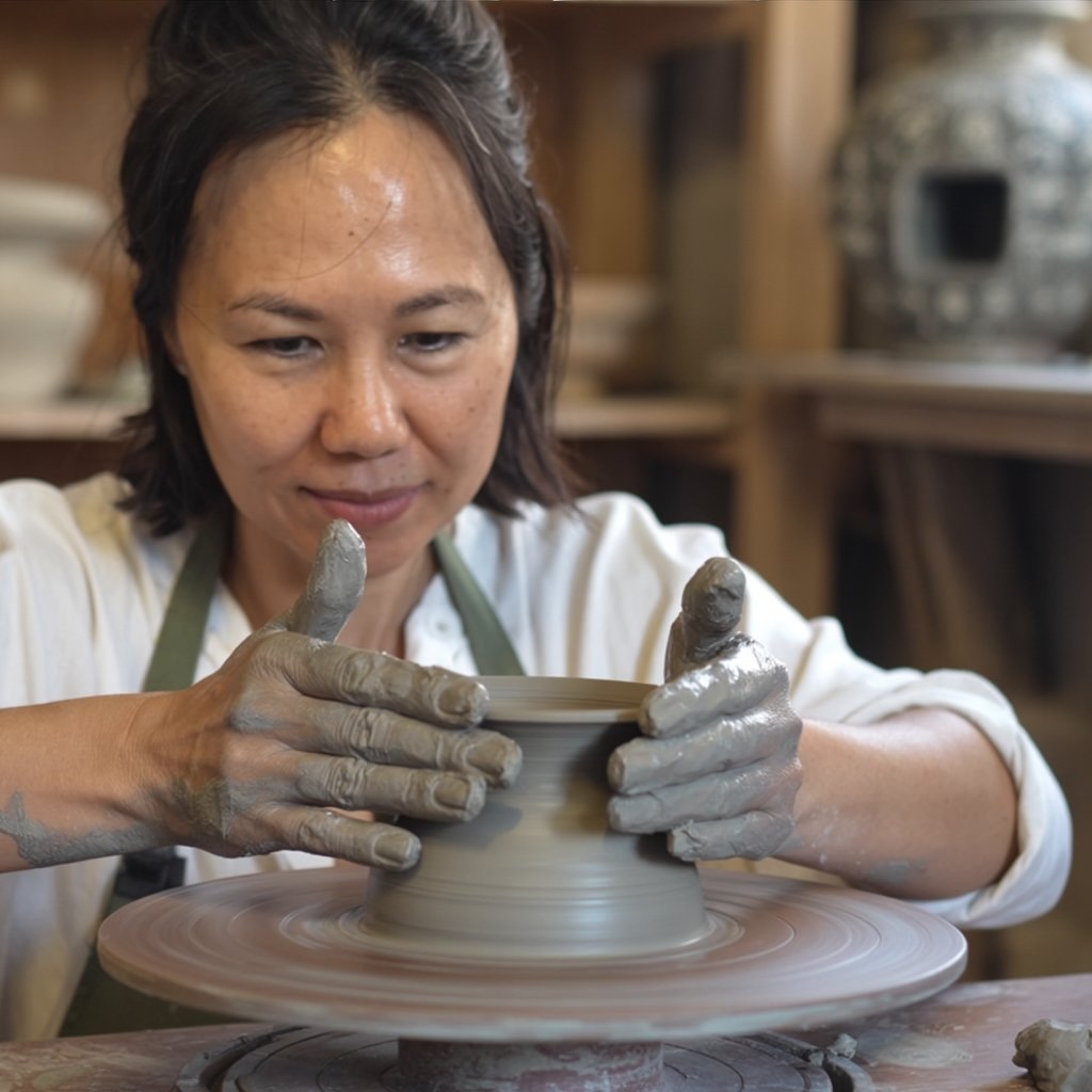 A woman shaping clay on a pottery wheel, focused and gently guiding the clay with her hands.