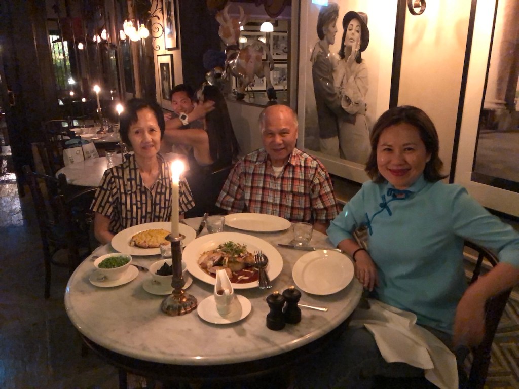A candid, candlelit photograph of the author and her parents smiling warmly together at a dinner table in an intimate restaurant setting, symbolizing their close family bond.
