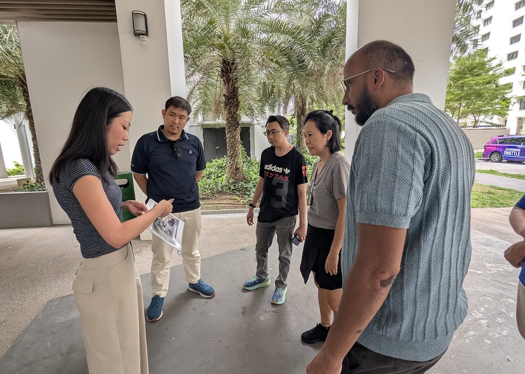 A group of participants, including Jane Bay, listening to a briefing from an official before boarding the autonomous shuttle trial.