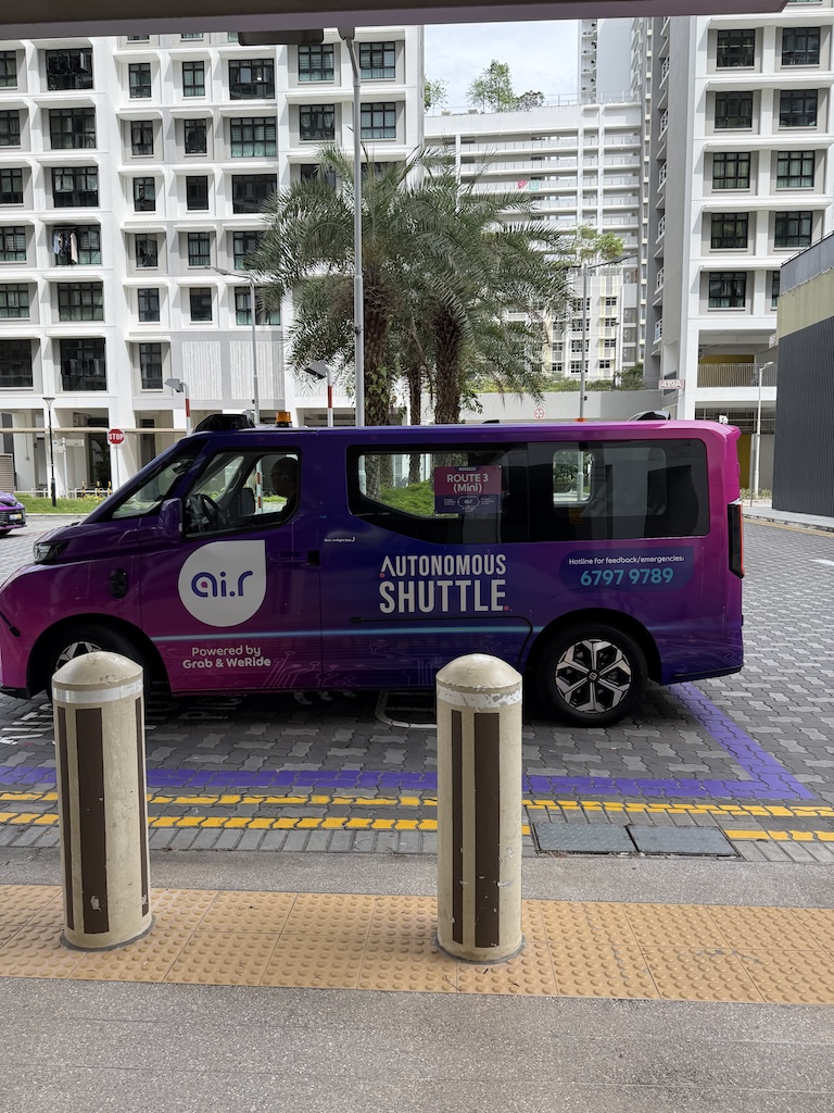 Side profile of a purple autonomous shuttle vehicle branded "ai.r" parked in a residential area of Singapore