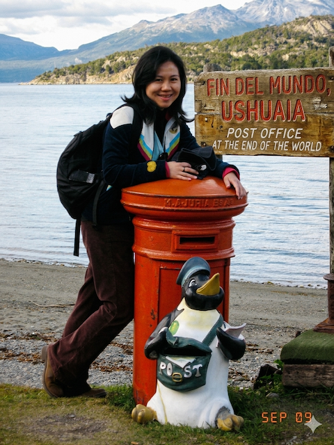A youthful Ageisano blogger leaning happily against the famous red "Fin del Mundo" (End of the World) post office box in Ushuaia, Argentina.