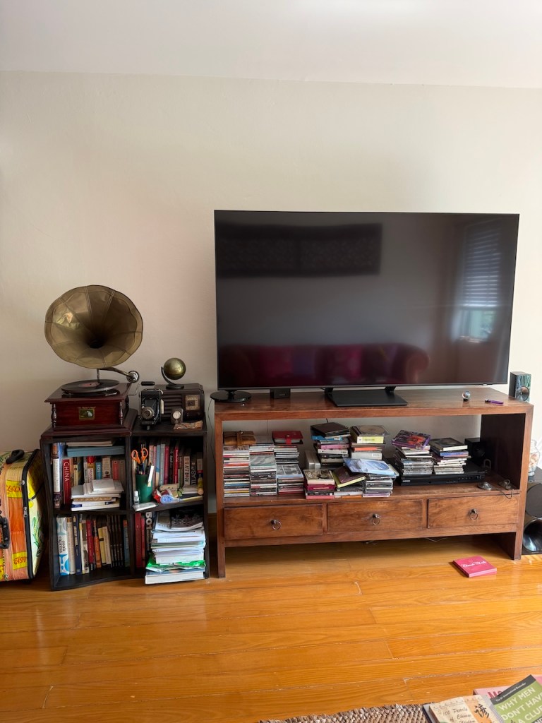 A wooden entertainment center filled with large stacks of music CDs and books during a home decluttering project.