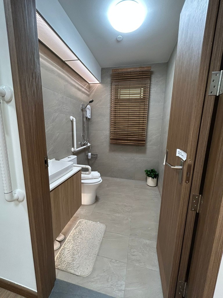 Interior photograph of an official HDB 2-room Flexi show flat bathroom featuring optional senior-friendly grab bars, universal design layout, and a flush-to-floor shower stall.
